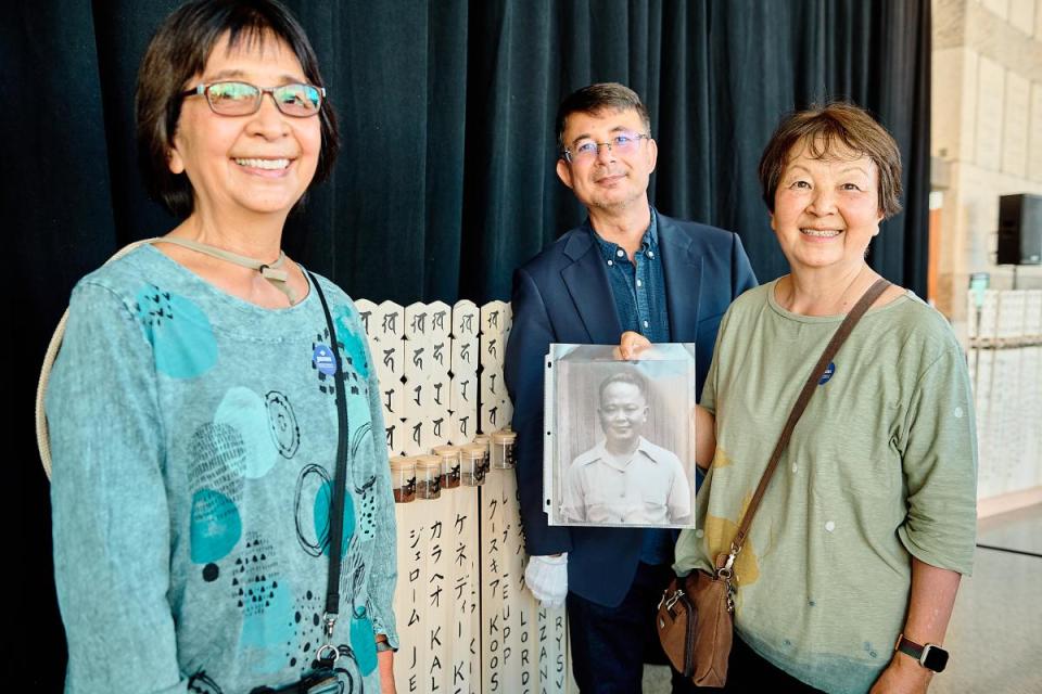 Visitors hold a photograph of a family member in front of the sotoba